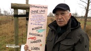 Ein älterer Herr steht neben einer Tafel mit dem Schriftzug "Dithmarschen ohne uns". © NDR 