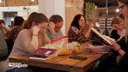 Junge Frauen sitzen in einem Raum an einem großen Tisch und lesen Bücher. © NDR 