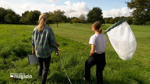 Zwei Frauen gehen mit einem Kescher über einen Golfplatz. © NDR Foto: NDR Screenshots