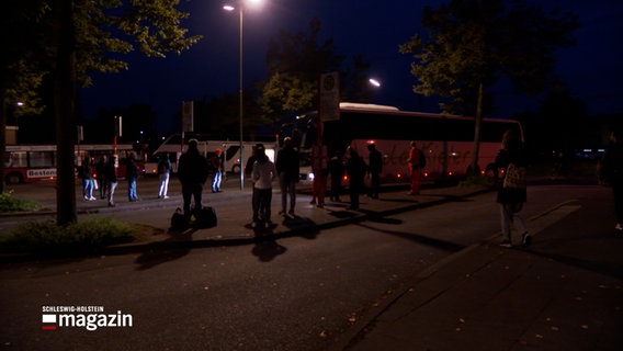 Mehrere Personen warten am frühen Morgen auf einen Bus. © NDR Foto: NDR Screenshots