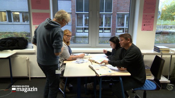 In einer Schule kommt ein lehrer an einen Tisch mit Schülern. © NDR Foto: NDR Screenshots