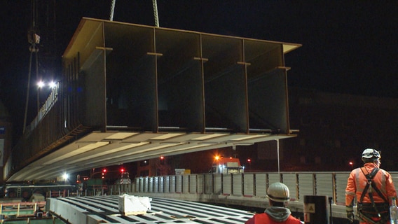 Ein 38 Meter langer Stahlträger wird mithilfe eines Krans auf einer Baustelle in Lübeck in Position gezogen © NDR 