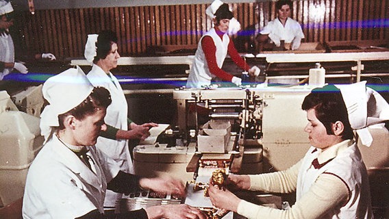 Ein historisches Foto zeigt Frauen in weißen Kitteln und Schürzen in der Trumpf-Schokoladenfabrik in Quickborn. © Geschichtswerkstatt Quickborn 