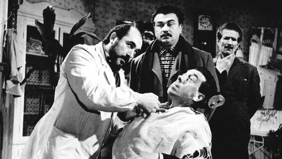 Mit Genuss beobachtet Peppone (Gino Cervi, Mitte), wie sein Lieblingsfeind Don Camillo (Fernandel, sitzend) versucht, sich dem Zahnarzt zu widersetzen. © NDR/Degeto 