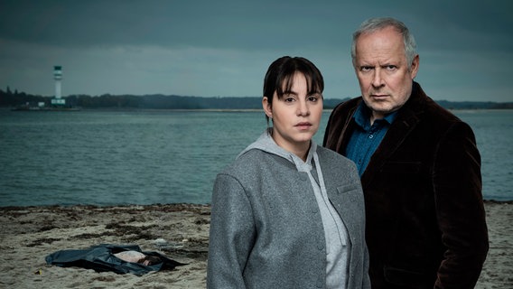 Sila Sahin (Almila Bagriacik) und Klaus Borowski (Axel Milberg) blicken in die Kamera, im Hintergrund Strand und Meer. © NDR/Thorsten Jander 