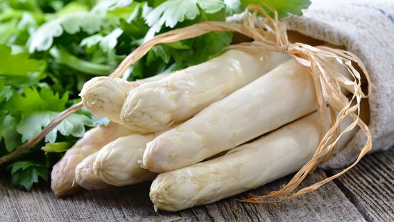 Frischer weißer Spargel und ein Bund Petersilie liegen auf einem Holztisch. © fotolia.com Foto: kab-vision