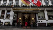 Haupteingang des Fairmont Hotel Vier Jahreszeiten in Hamburg. Davor steht ein Concierge im roten Sakko. © picture alliance / Eibner-Pressefoto | Eibner-Pressefoto 