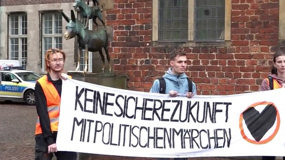 Aktivisten der "Letzte Generation" protestieren mit einem Plakat vor den Bremer Stadtmusikaten. Die Statue ist mit schwarzer Farbe beschmiert. © Nord-West-Media TV 