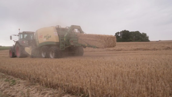 Traktor zieht eine Strohballenpresse, ein Großballen kommt hinten heraus. © NDR 