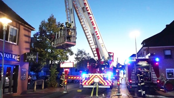 Einsatzkräfte der Feuerwehr stehen mit einem Drehleiter in Syke, um einen Hausbrand zu löschen. © Nord-West-Media TV 