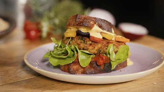 Ein dick mit Salat, Bulette und Gemüse belegter vegetarischer Burger liegt auf dem Teller. © Screenshot Foto: Moritz Schwarz/Oliver Zydek