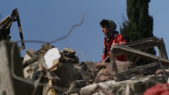 Nach dem Erdbeben in der Türkei steht ein junger Mann hinter Trümmern. © NDR/Kinescope Film Foto: Thorsten Bartels