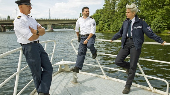 An Bord der Silbermöwe tauschen Wolf Malletzke (Christoph Grunert, l.), Fahri Celik (Hassan Akkouch, M.) und Marlene Weber (Oska Melina Borcherding, r.) die neuesten Erkenntnisse aus, die sie gerade im Umweltaktivst*innen-Camp gesammelt haben. © ARD/Daniela Incoronato 