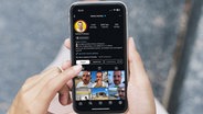 Eine Frau hält ein Smartphone in den Händen auf dem das Instagram-Profil eines Immobilien-Influcencers zu sehen ist. © Colourbox / Screenshot Instagram Foto: Colourbox