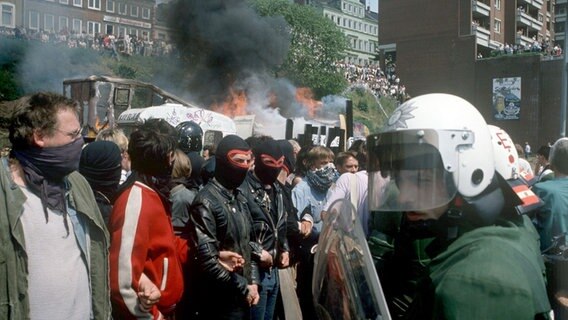 Vermummte Hausbesetzer und Sympathisanten und Ordnungshüter stehen sich am 26.05.1989 vor brennenden Bauwagen gegenüber © picture alliance / dpa 