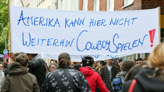 Angehörige und Freunde des in den USA erschossenen Austauschschülers Diren aus Hamburg nehmen am 02.05.2014 in Hamburg an einem Trauermarsch teil und tragen ein Transparent mit der Aufschrift "Amerika kann hier nicht weiterhin Cowboy spielen". © picture alliance / dpa Foto: Bodo Marks