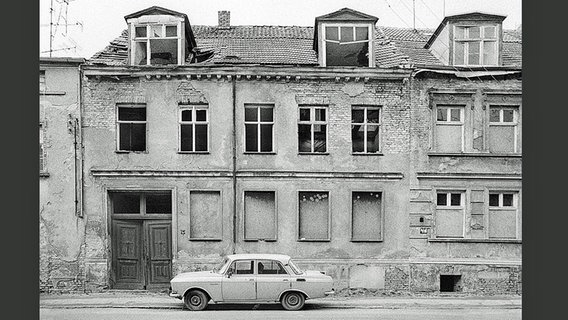 Ein Moskwitsch-Auto steht vor einem Gebäude mit zugenagelten Fenstern. © Robert Conrad 