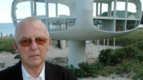 Der Architekt Ulrich Müther (1934-2007) am 7. Juli 2004 vor dem von ihm selbst in den 70er-Jahren konstruierten und 1981 aufgestellten futuristisch anmutenden Rettungsturm im Ostseebad Binz. © picture-alliance / dpa Foto: Stefan Sauer