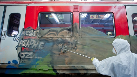 Ein Mitarbeiter reinigt am 14. Oktober 2014 in Hamburg im S-Bahn Werk in Ohlsdorf einen mit Graffiti bemalten Waggon. Links steht "Rest in peaphe OZ...". © picture alliance / dpa Foto: Daniel Bockwoldt