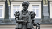 Ein Denkmal erinnert auf dem Marktplatz von Annaberg-Buchholz an Barbara Uthmann. Die Verlegerin beschäftigte im 16. Jahrhundert bis zu 900 Bortenwirkerinnen und hat maßgeblich zur Verbreitung des Klöppelns im Erzgebirge beigetragen. © picture alliance/dpa Foto: Hendrik Schmidt