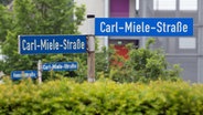 Ein Straßenschild "Carl-Miele-Straße" ist vor dem Firmengelände der Miele & Cie. KG zu sehen. An dem Hauptsitz in Gütersloh produziert Miele seine Waschmaschinen und Waschtrockner. © picture alliance/dpa Foto: Friso Gentsch