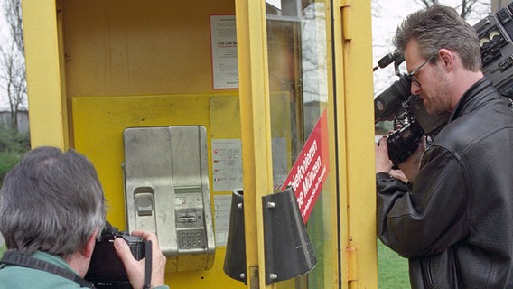 Ein Kamermann und ein Fotograf stehen am 22. April 1994 vor der Telefonzelle im Berliner Stadtteil Treptow, in der nach Polizeiangaben der Kaufhauserpresser "Dagobert" (Arno Funke) festgenommen wurde. © dpa-Bildfunk Foto: Bernd Settnik