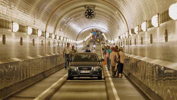 Ein Auto fährt durch eine Röhre des Alten Elbtunnels, auf den Gehwegen zu beiden Seiten der Fahrspur gehen Menschen. © picture alliance / Caro Foto: Bastian