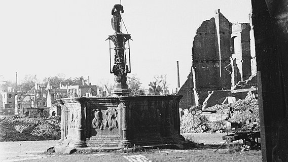 Hildesheim nach den Luftangriffen vom 22. März 1945: Blick aus einer Rathaus-Arkade auf den kopflosen Stadtsoldaten auf dem Marktbrunnen, dahinter links die Schutthaufen des Knochenhauer-Amtshauses und rechts der Stadtschenke © Theo Wetterau/Verlag Gebrüder Gerstenberg Foto: Theo Wetterau