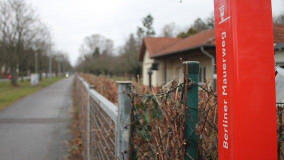 Blick über den Zaun des Friedhofs Pankow, am Rand ein Schild mit der Aufschrift "Berliner Mauerweg". © NDR Foto: Daniel Sprenger