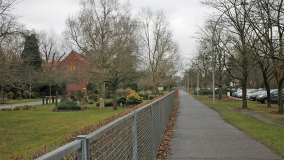 Blick über den Zaun am Friedhof Pankow, links davon eine Rasenfläche an der Stelle früherer Gräber, rechts ein Fußweg. © NDR Foto: Daniel Sprenger