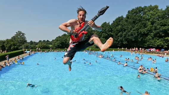 Benni (33) aus Dortmund springt am 01.08.2014 in Wacken (Schleswig-Holstein) im Schwimmbad mit einer aufblasbaren Gitarre vom Drei-Meter-Turm ins Wasser. © picture alliance / dpa Foto: Axel Heimken