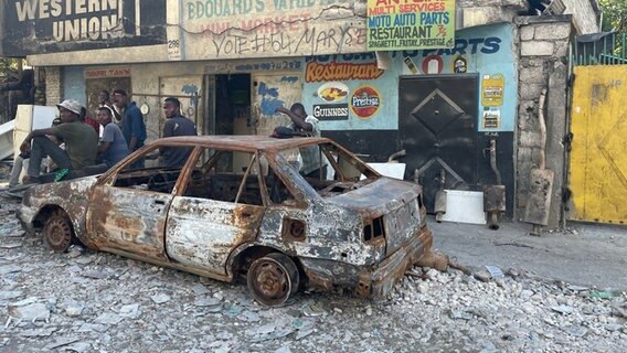 Jugendliche sitzen auf einem ausgebranntem Auto im Stadtteil Carrefour-Feuilles auf Haiti © NDR Foto: Anne Demmer