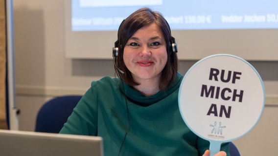 Katahrina Fegebank hält beim "Hand in Hand"-Spendentag ein Schild mit der Aufschrift "Ruf mich an" in die Kamera. © NDR/Janis Roehlig Foto: Janis Roehlig