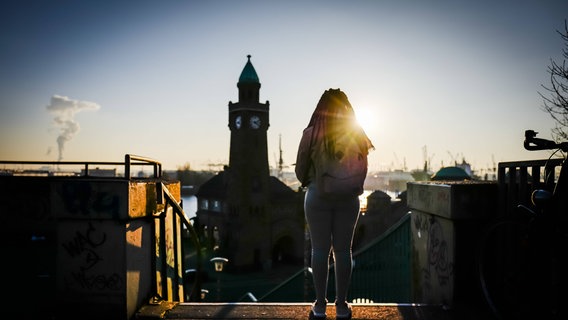 Eine Frau steht bei sonnigem Winterwetter allein in der Nähe der Landungsbrücken und blickt auf die Elbe. © Imago Foto: Lars Berg