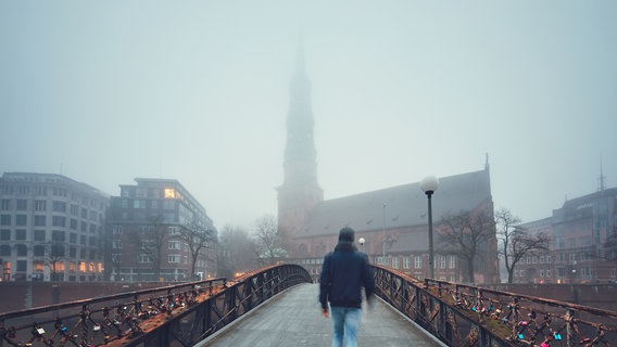 Ein Mann läuft über eine Brücke im Nebel. © IMAGO / Dreamstime 