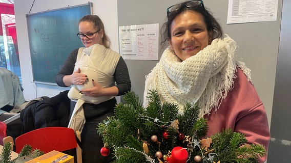 Zwei Frauen, eine von ihnen hat ein Baby auf dem Arm, sind beim Proket "Zeit für mich" und haben Adventsschmuck in der Hand. © NDR Foto: Stefanie Wittgenstein