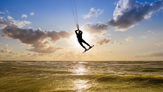 Ein Kiter fliegt über dem Meer im Gegenlicht. © COLOURBOX Foto: Frank Peters