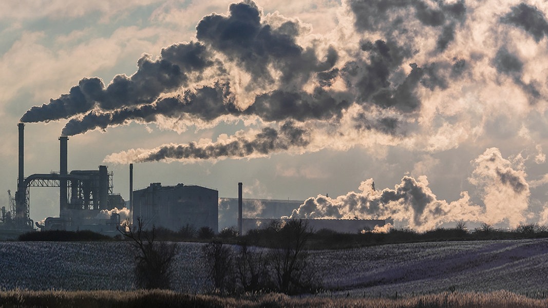 Dunkler Rauch steigt aus Schornsteinen einer Industrieanlage.