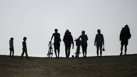 Menschen in einer Gruppe stehen im Gegenlicht auf einer erhöhten Rasenfläche. © imago-images Foto: photothek