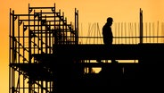 Bauarbeiter geht auf einer Baustelle für ein Gebäude am Kronberg, während die Sonne aufgeht. Die Tarifverhandlungen im Baugewerbe sind wegen dem Coronavirus verschoben. © dpa-Bildfunk Foto: Julian Stratenschulte/dpa