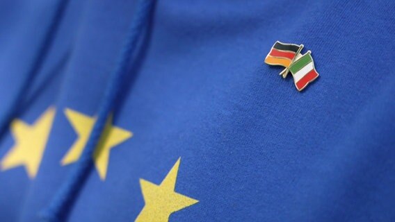An einer Europaflagge hängen zwei weitere Länderflaggen: Deutschland und Italien. © NDR 
