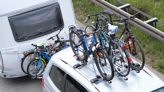Fahrräder auf einem Fahrzeugdach und am Wohnwagen befestigt. © dpa-Bildfunk Foto: Peter Steffen/dpa