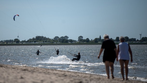 Spaziergänger laufen über den Strand Hooksiel, als Kitesurfer mit ihren Drachen unterwegs sind. © dpa-Bildfunk Foto: Sina Schuldt/dpa