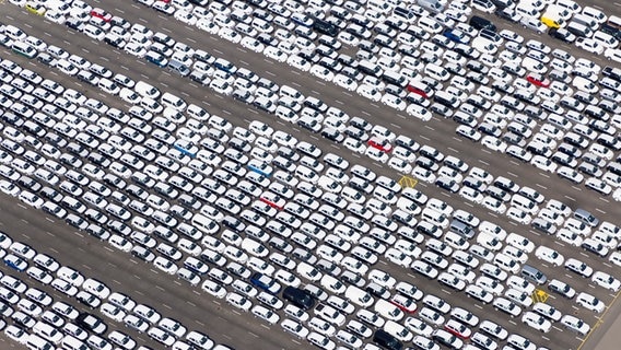 Blick auf fertig produzierte Fahrzeuge, die auf einem großen Parkplatz vor dem Volkswagenwerk auf die Verschiffung warten. © picture alliance/dpa Foto: Tobias Bruns