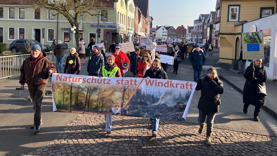 Mehrere Menschen laufen mit Trillerpfeifen und einem großen Plakat mit der Aufschrift "Naturschutz statt Windkraft" auf einer Straße in Winsen (Luhe). © NDR Foto: Kai Rake