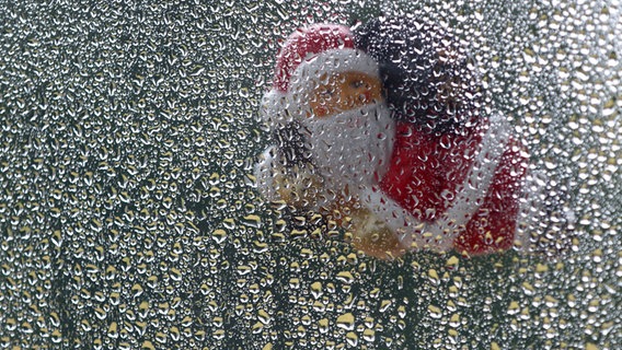 Eine Weihnachtsmannfigur hängt vor einem Fenster mit Regentropfen. © picture alliance / Jens Büttner/dpa-Zentralbild/dpa Foto: Jens Büttner