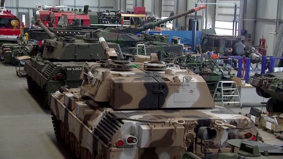 In einer Halle des Flensburger Unternehmen FFG stehen zahlreiche Leopard-1-Panzer, im Hintergrund stehen andere rote Fahrzeuge. © ZDF 