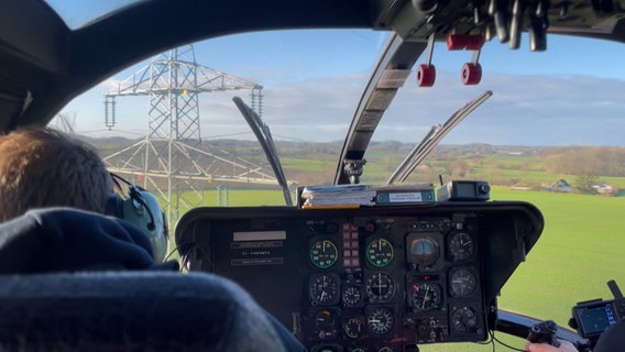 Ein Helikopter schwebt vor einem Strommast. © NDR 