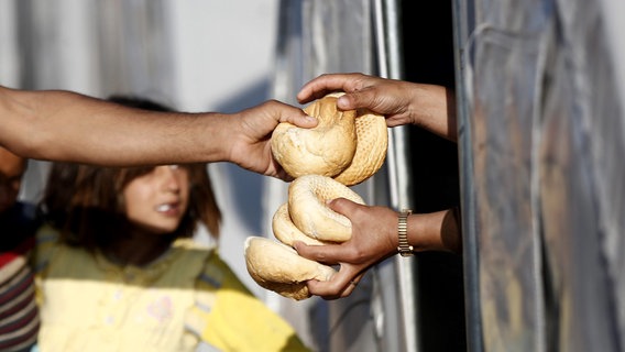 Hände reichen Brötchen aus einem Zelt heraus, ein anderes Paar Hände greift sie. © picture alliance / dpa | Sedat Suna Foto: Sedat Suna