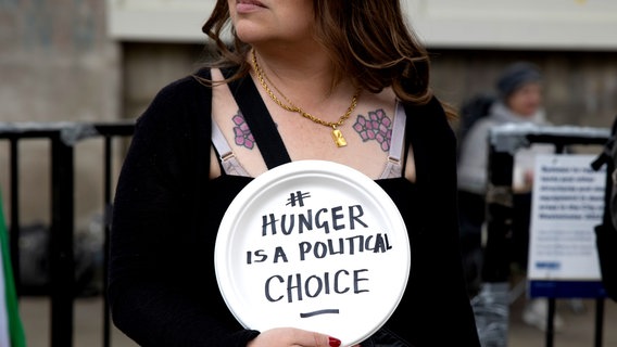 Eine Frau hält bei einer Demonstration ein Schild hoch mit der Aufschrift: "Hunger is a political Choice". © picture alliance / ZUMAPRESS.com | Hesther Ng Foto: Hesther Ng